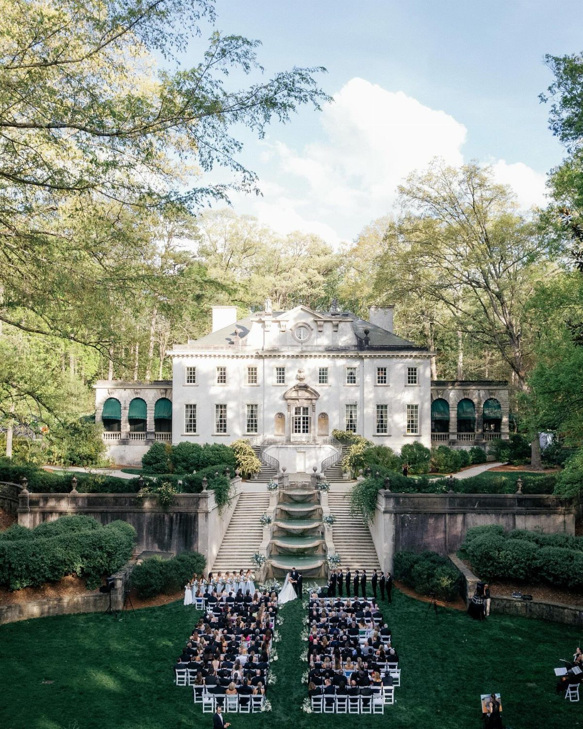 White historic mansion with terraced gardens and cascading fountain during an outdoor wedding.