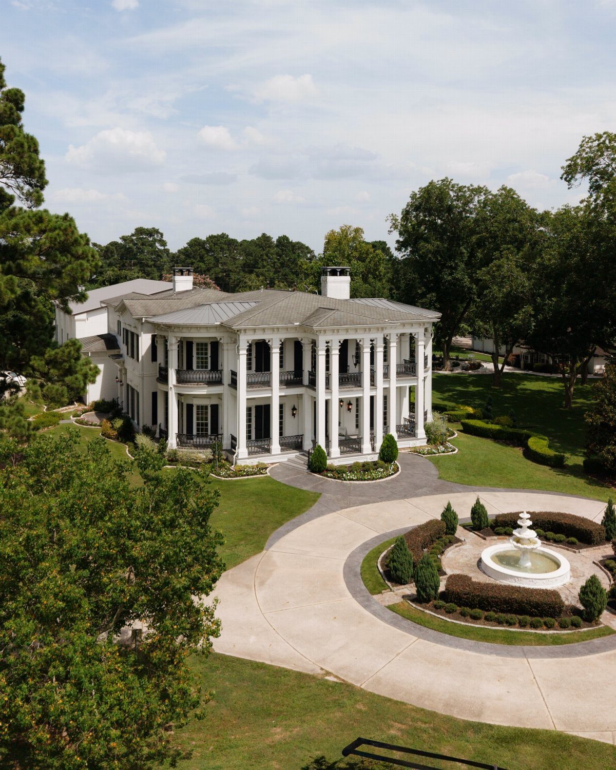 White neoclassical mansion with a curved colonnade, circular driveway, and central fountain.