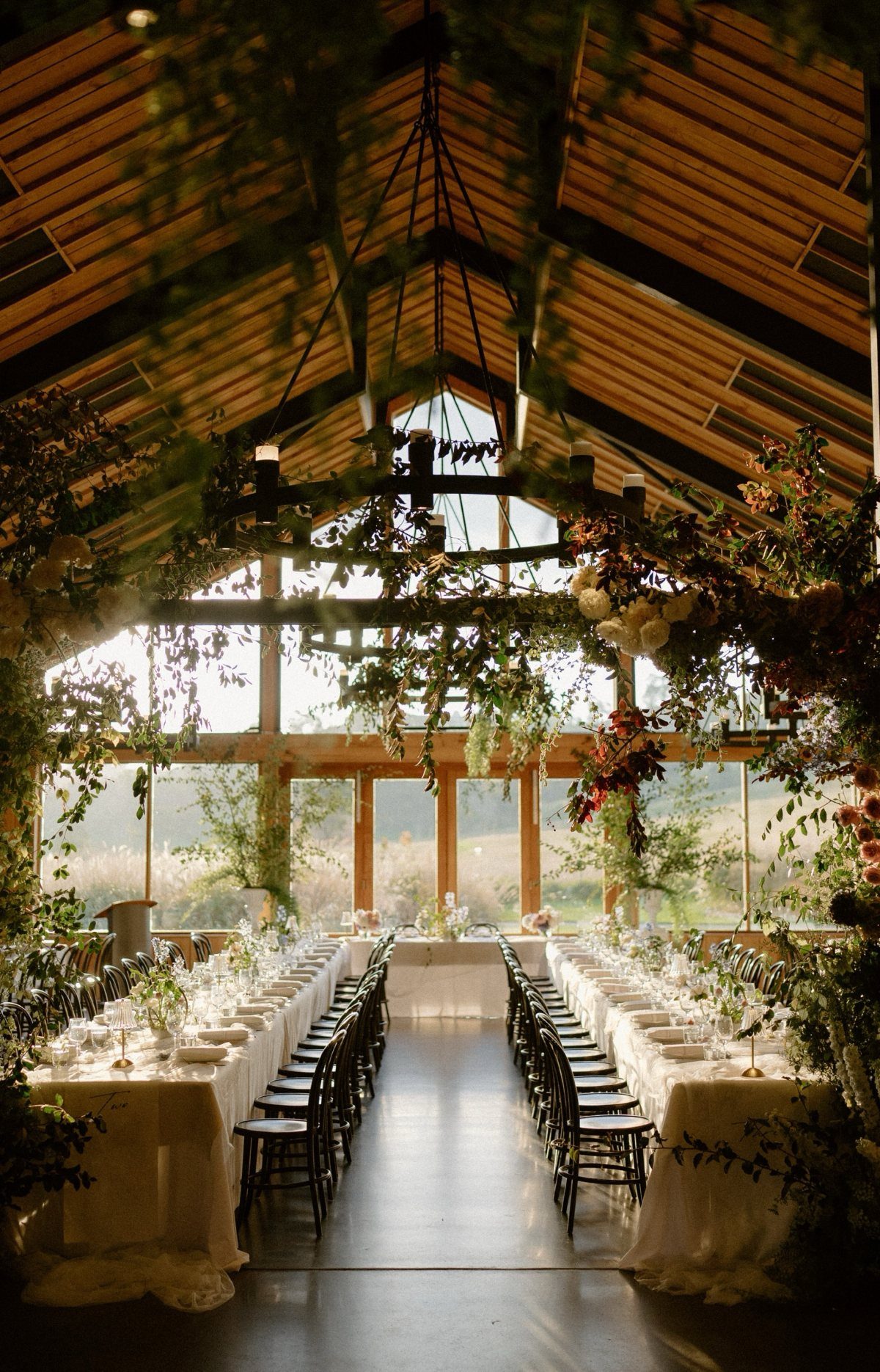 Wedding banquet table in a rustic hall with vaulted wooden ceilings and greenery.