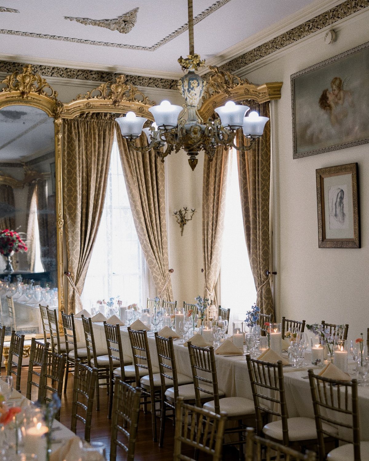 Formal dining room with gold accents, ornate chandelier, and long banquet table setup.