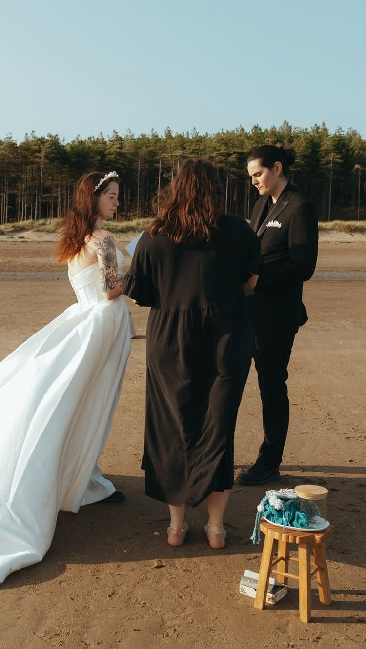 Couple in wedding attire standing with an officiant on a sandy beach