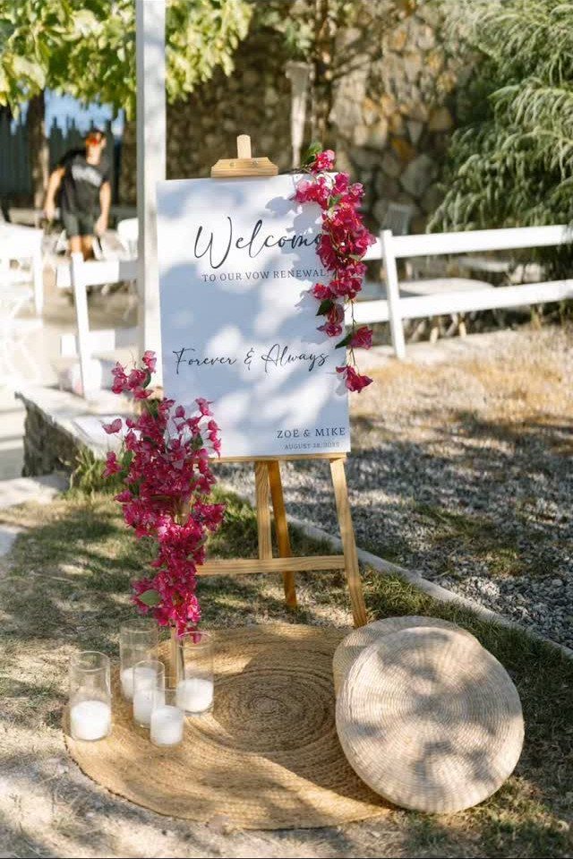 Welcome sign for vow renewal decorated with pink flowers and straw accessories outdoors