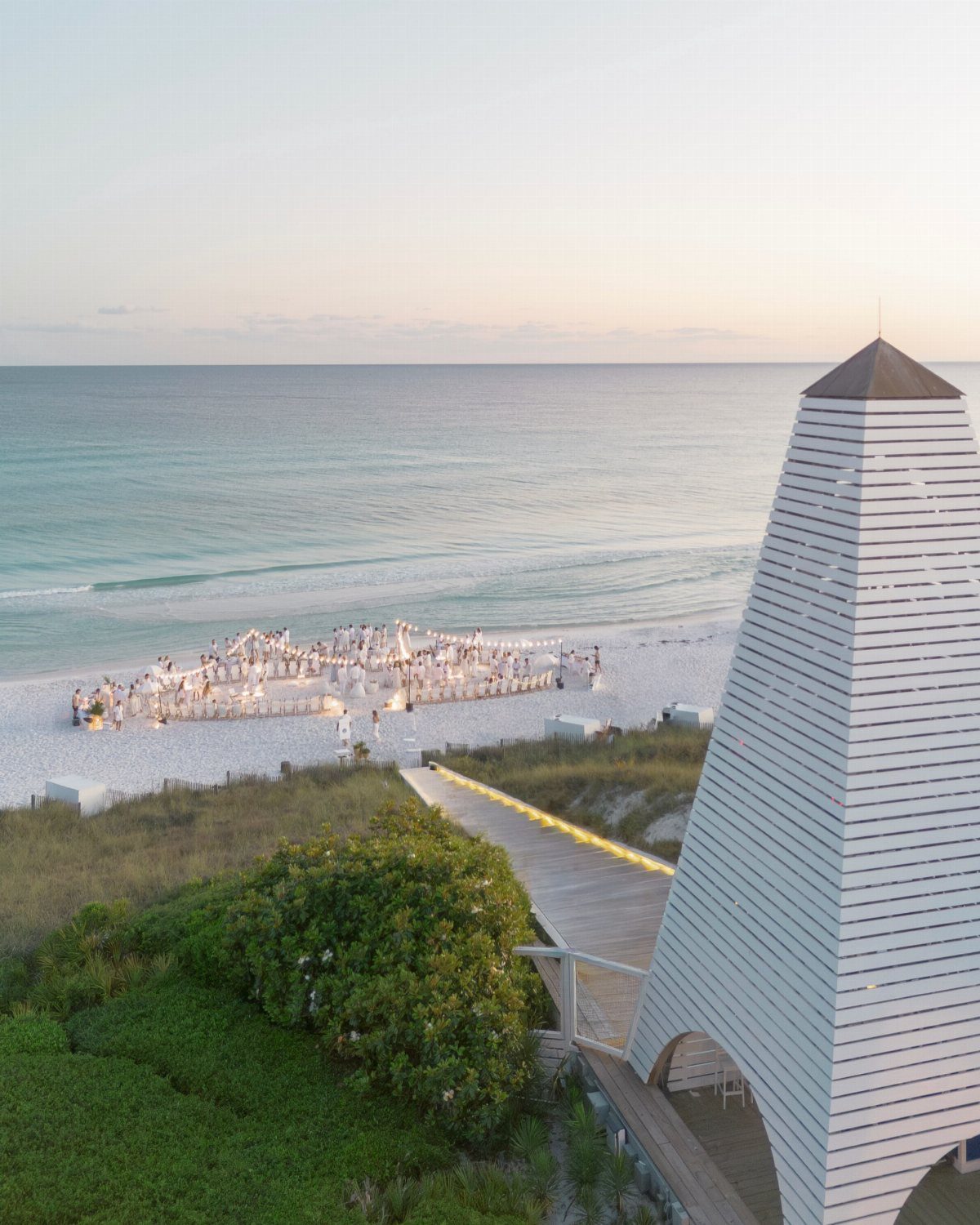 Beach wedding ceremony with guests in white on white sand by the ocean.