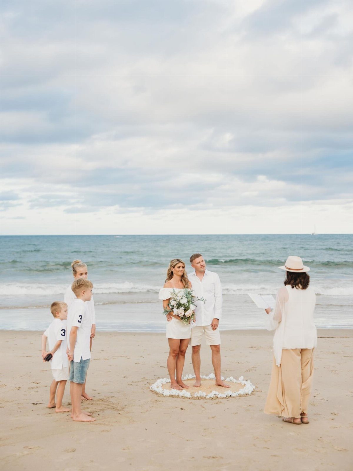 Bride and groom standing barefoot on a sandy beach during their wedding ceremony.