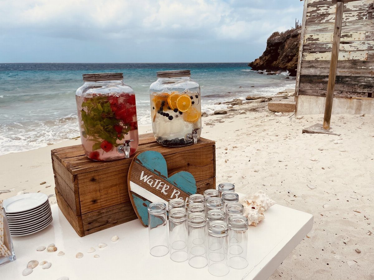 Beverage dispensers with fruit and glasses on a white table at the beach