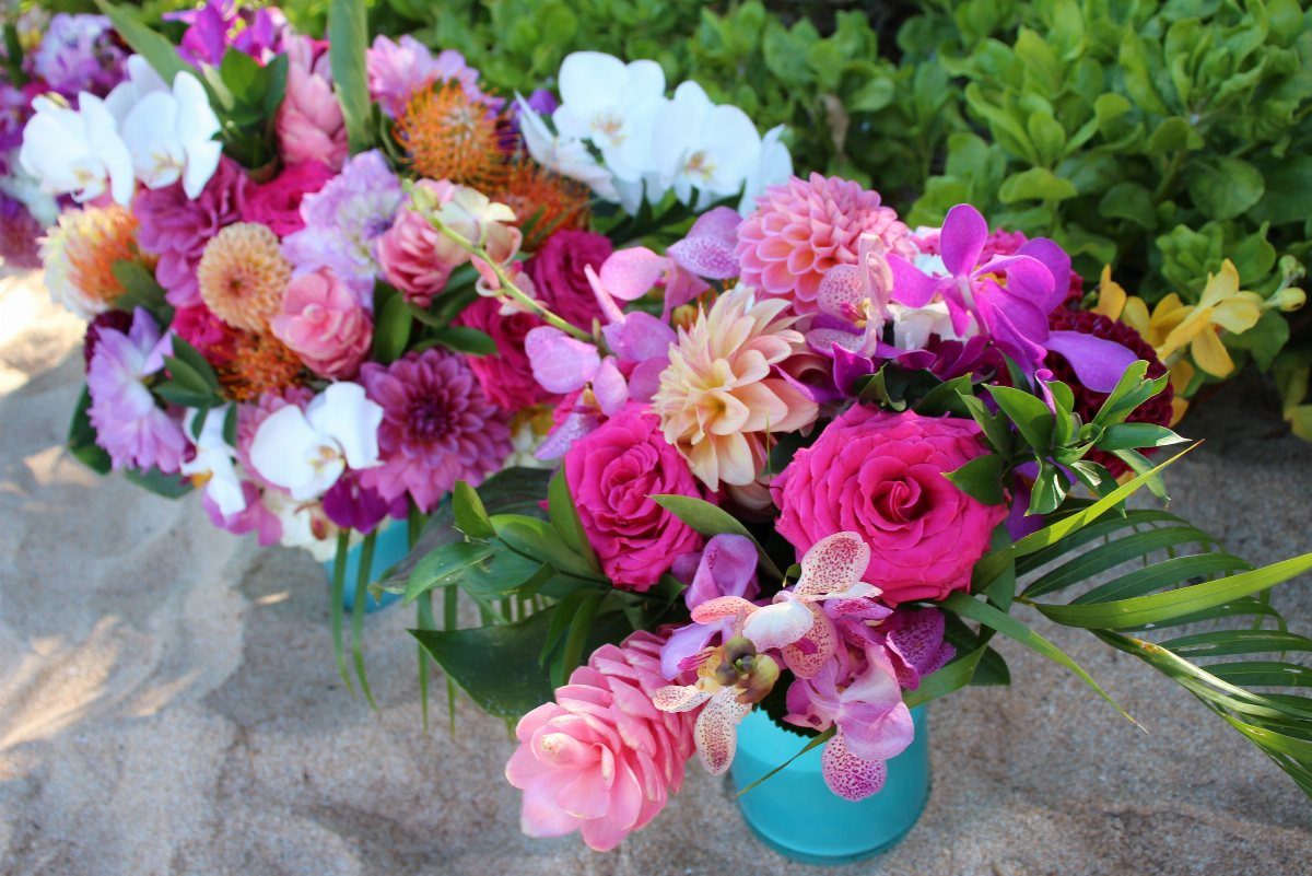 Colorful wedding bouquets with pink and purple flowers sitting on sandy beach ground.