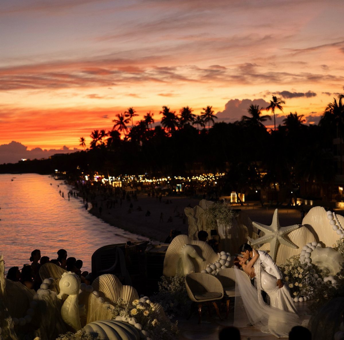 Couple embracing at a beach wedding with shell decorations during a vibrant sunset