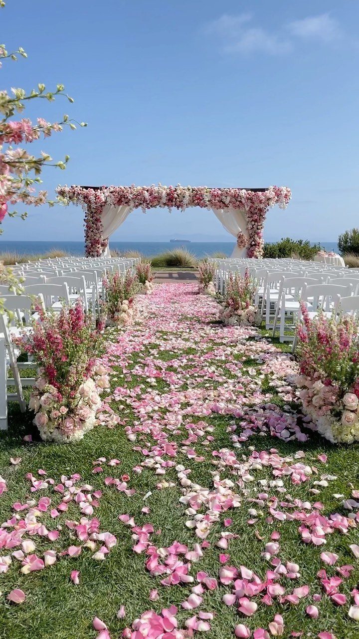 Outdoor wedding ceremony setup with pink petal aisle and floral arch by the ocean