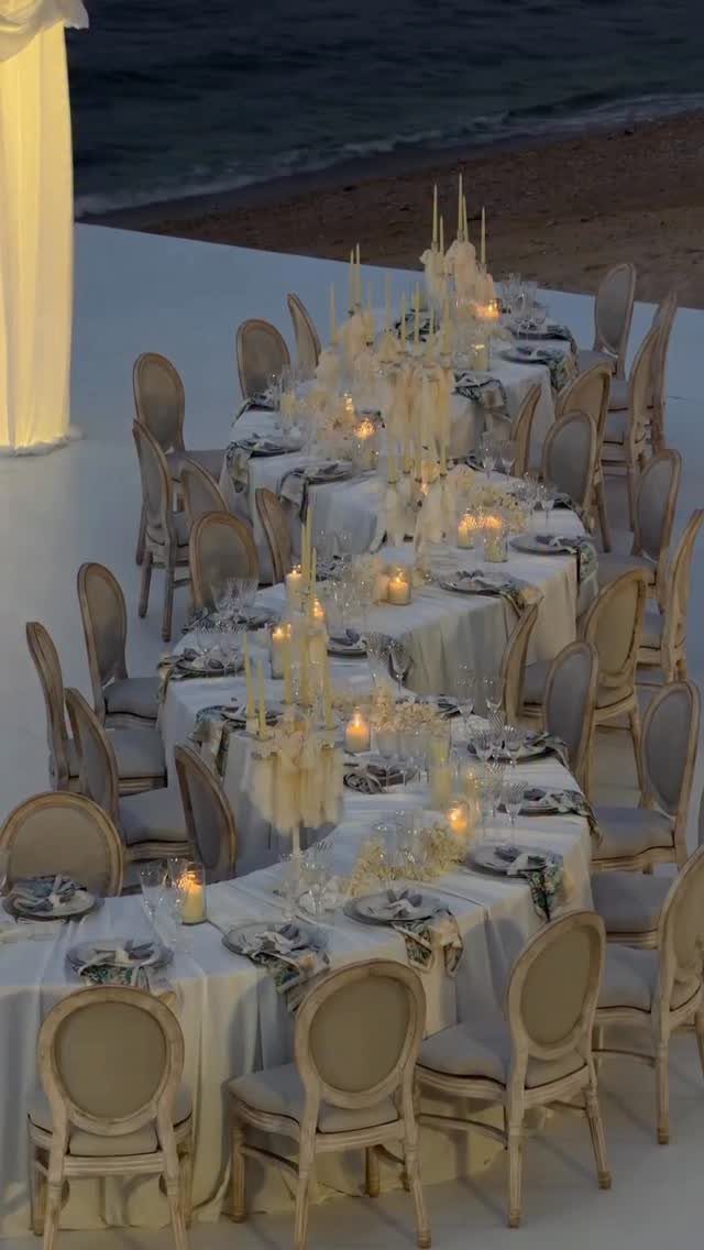 Elegant wedding reception tables with candles on a terrace overlooking a beach at dusk