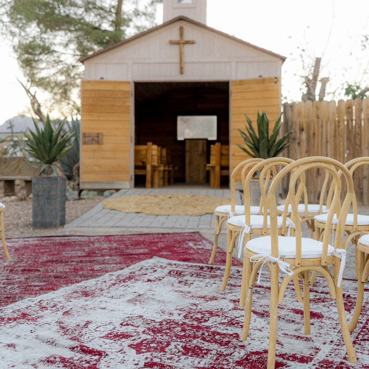 Small wooden chapel with a cross and rows of chairs on patterned rugs.