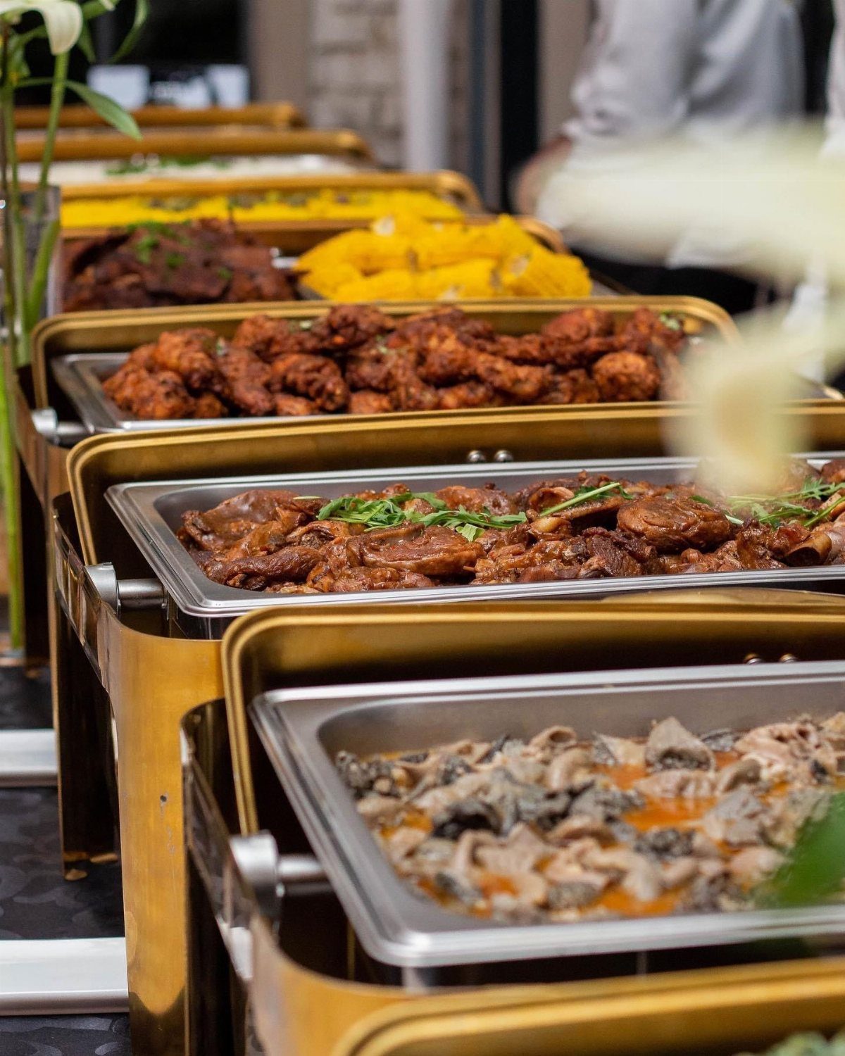 Gold buffet chafing dishes filled with various meats and vegetables at a wedding.