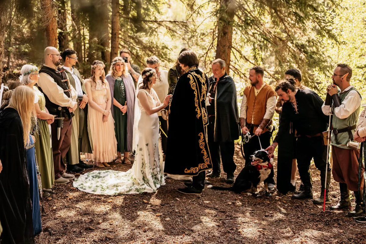 Couple and guests in medieval-style attire during a forest wedding ceremony.