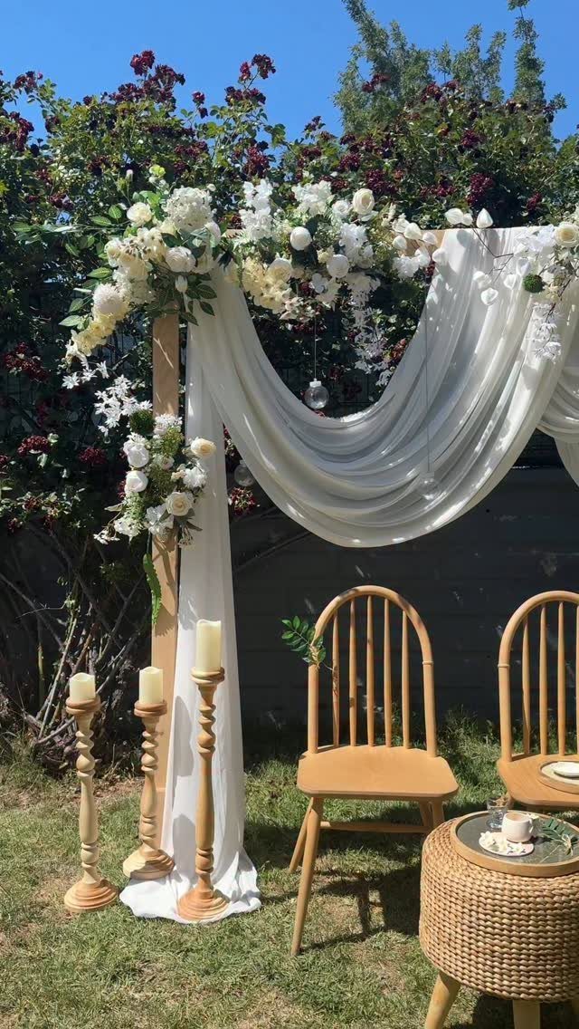 Wedding altar with white fabric and flowers set up in a grassy backyard