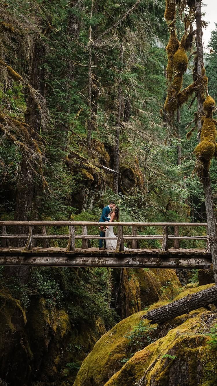 Couple in wedding attire kissing on a wooden bridge in a mossy forest