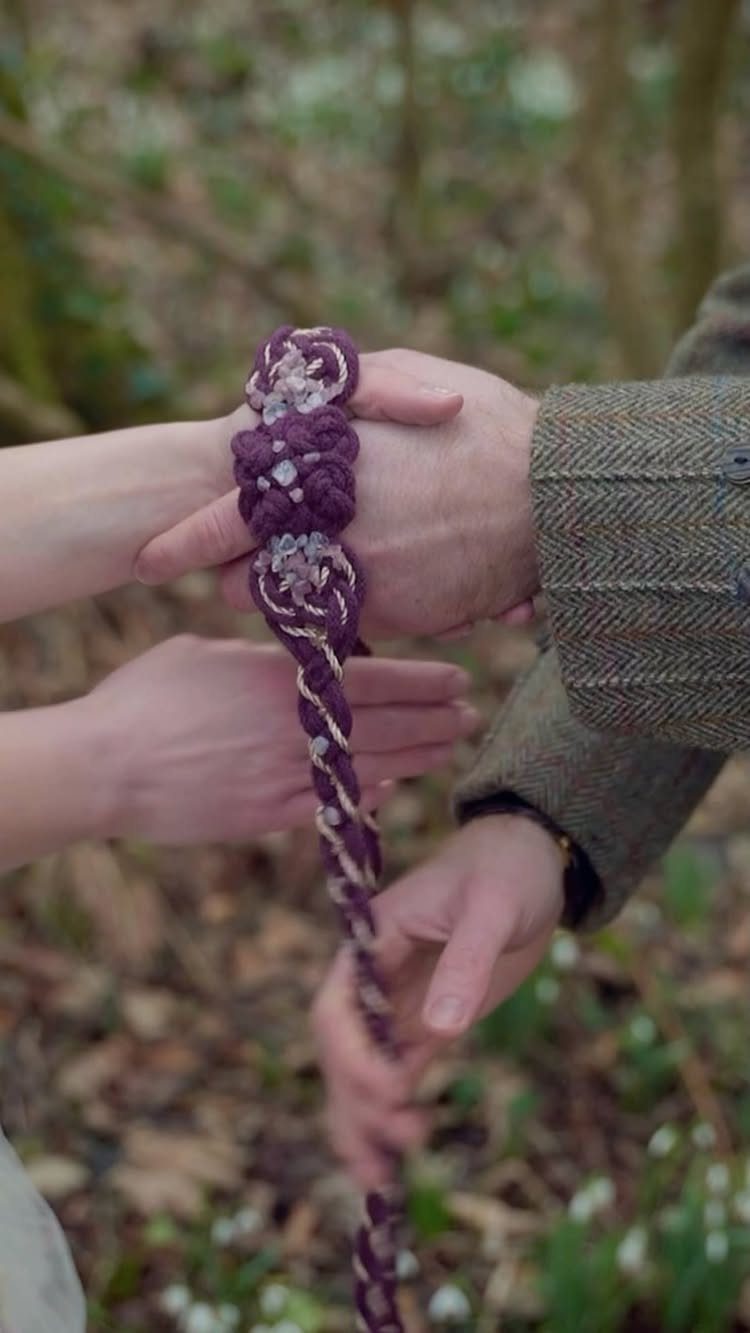 Hands of a couple tied together with a braided purple cord in woods