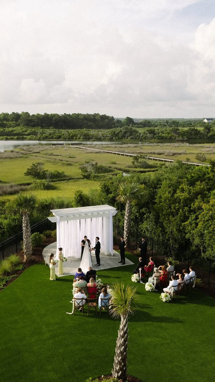Small wedding ceremony with a few guests under a white pergola overlooking a marsh.