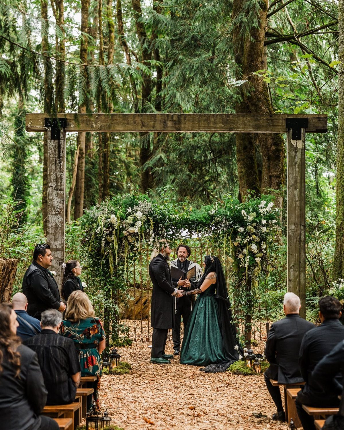 Couple marrying under a wooden arbor in a forest with guests watching