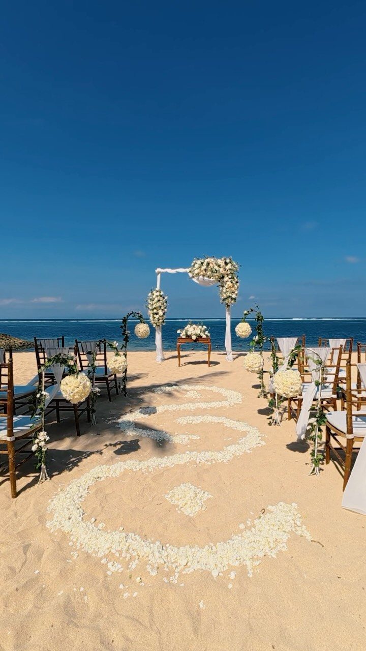 Beach wedding ceremony setup with floral arch and chairs on sandy shore