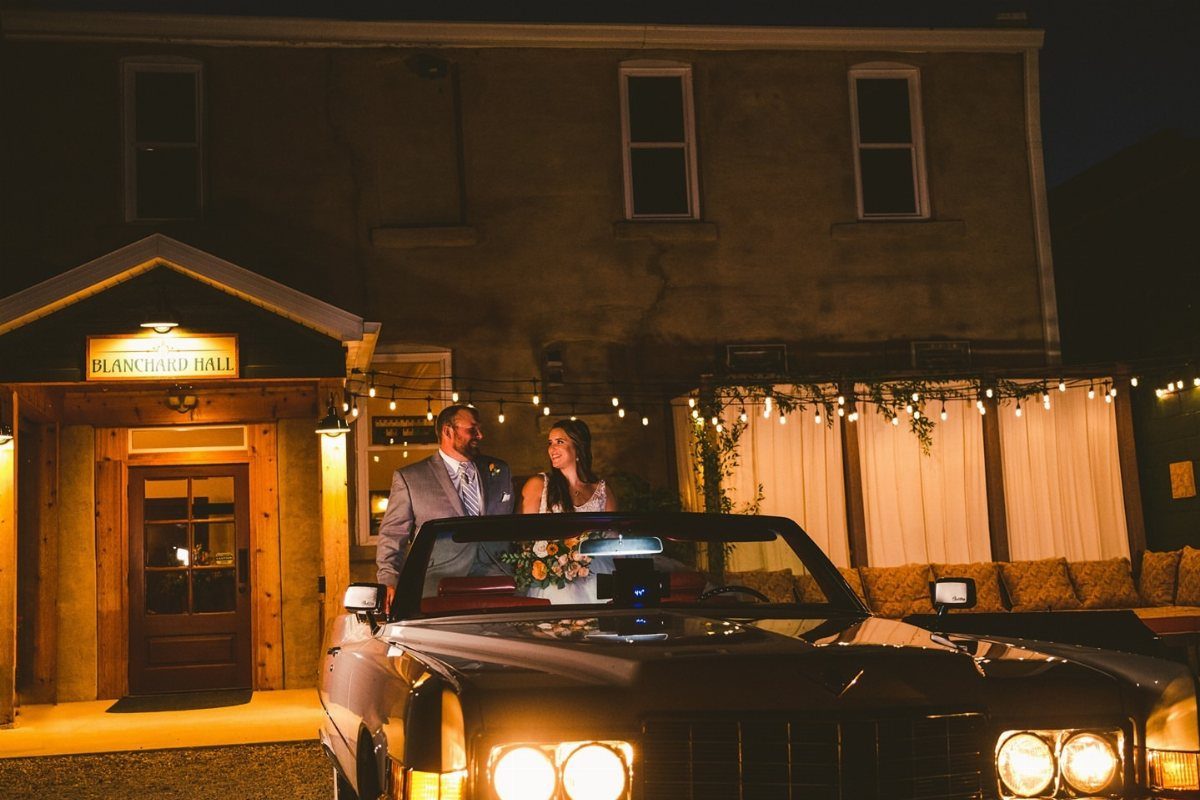 Bride and groom standing by a vintage car outside Blanchard Hall at night.