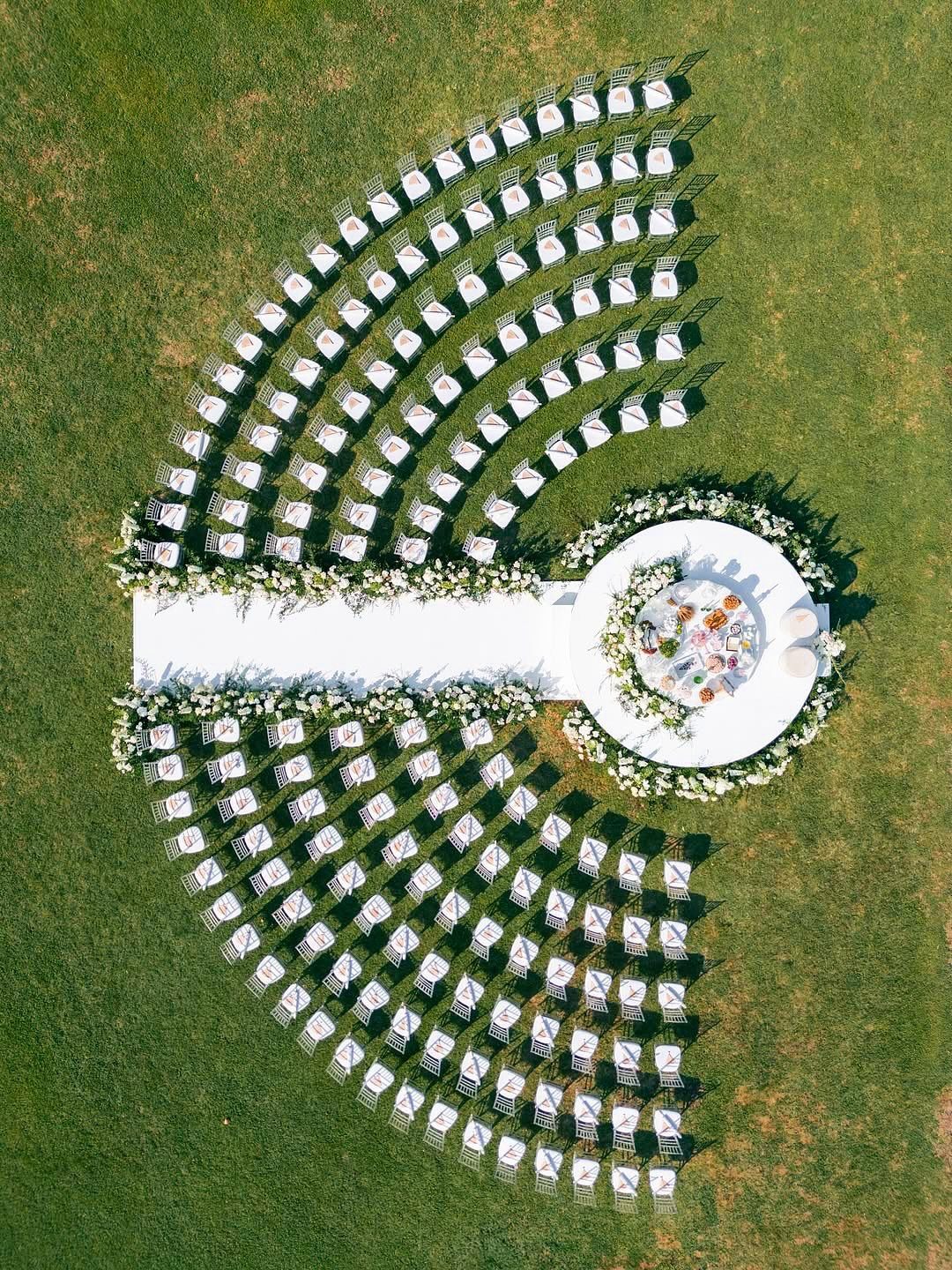 Outdoor wedding ceremony setup with curved white chairs and a circular floral platform.