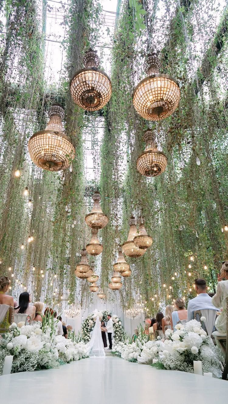 Lavish wedding ceremony venue with hanging greenery, gold chandeliers, and white floral aisle.