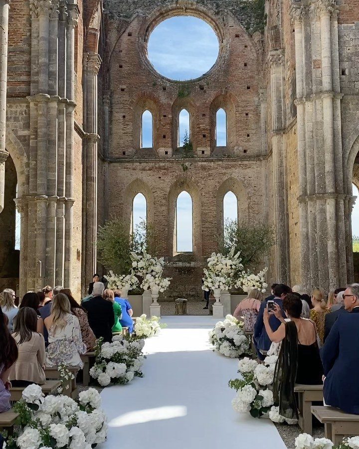 Wedding ceremony aisle with white flowers inside ancient stone cathedral ruins.