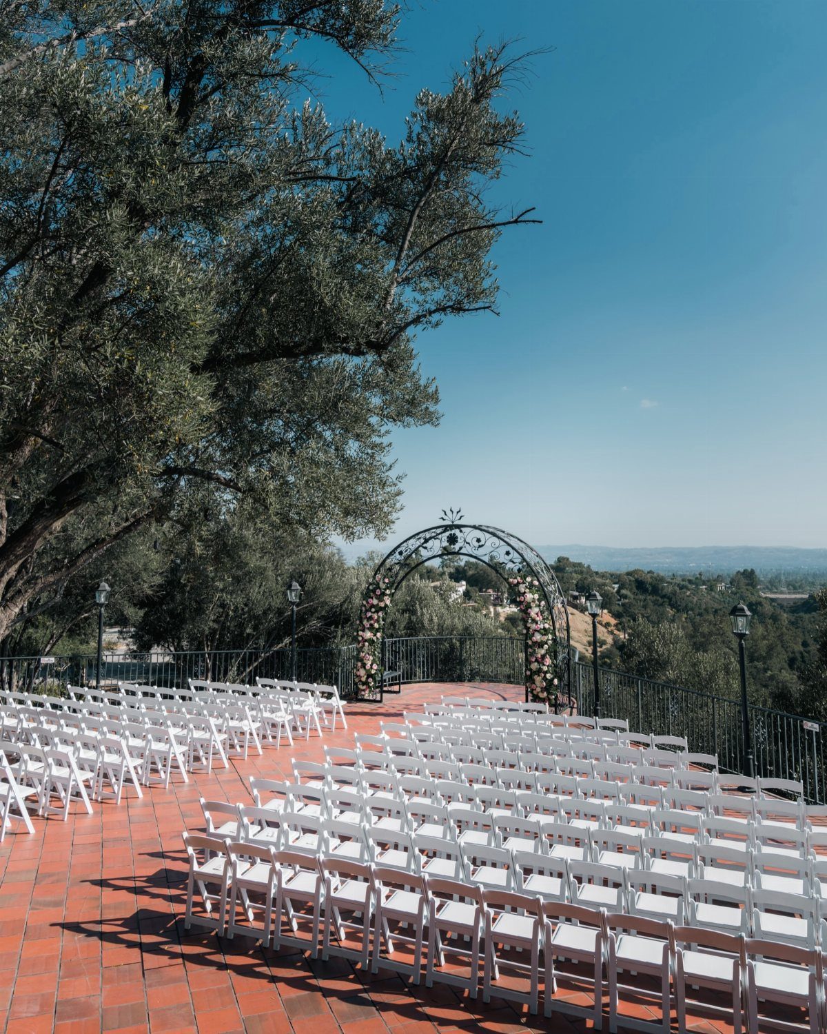 White wedding chairs on a terracotta patio facing a floral arch and valley view.