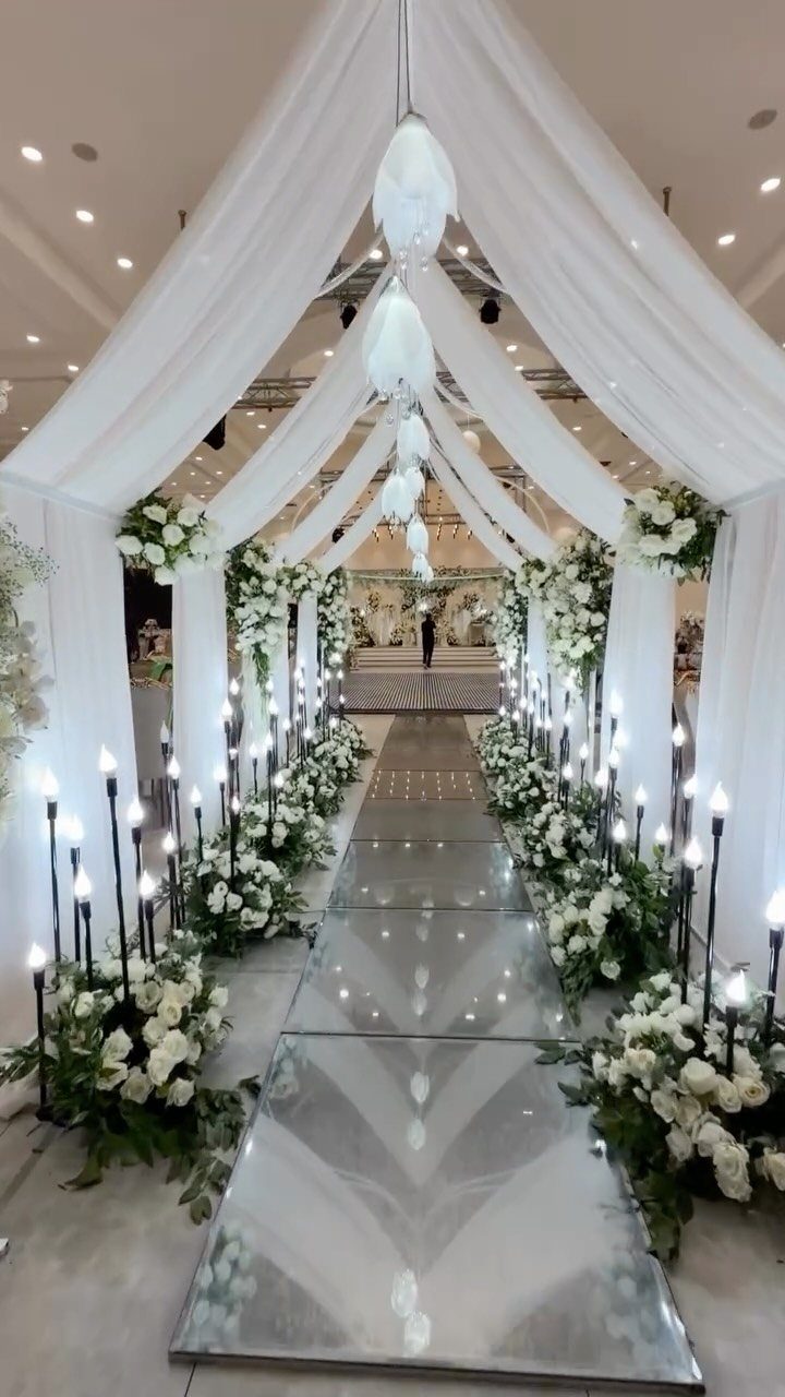 Mirrored wedding aisle with white flowers, black candles, and white fabric ceiling draping.