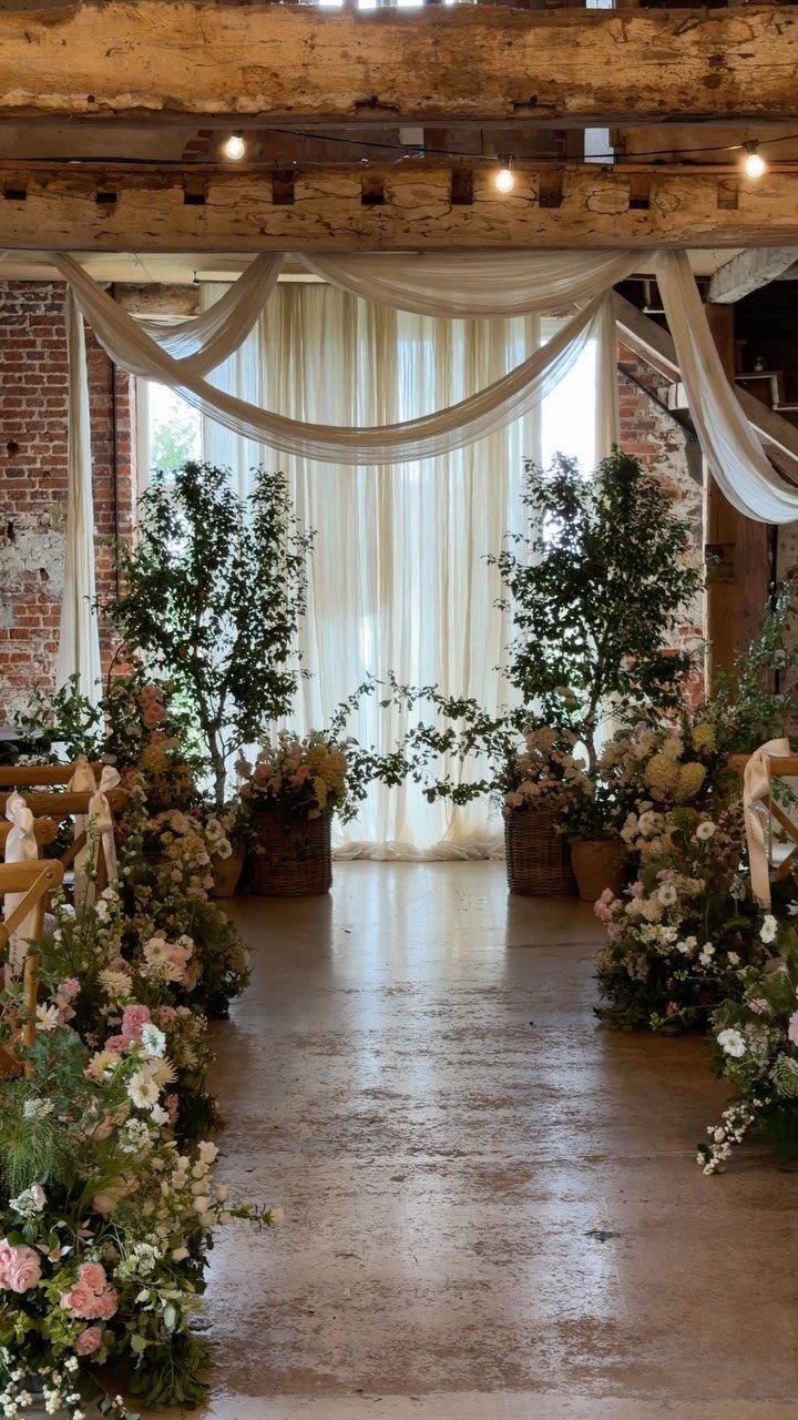 Rustic wedding ceremony venue with floral aisle, white draping, and exposed wooden beams.