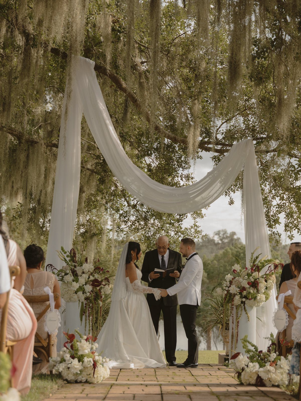 Bride and groom during an outdoor wedding ceremony under a mossy oak tree.