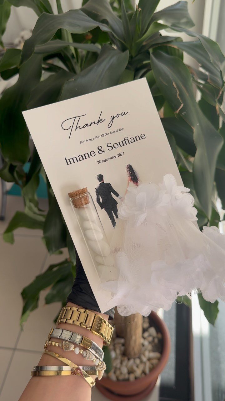 Wedding thank you card with a small glass bottle and white fabric flowers.
