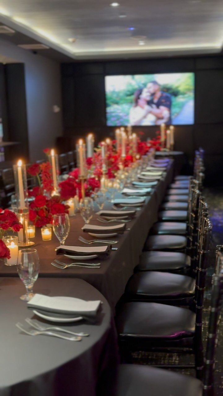 Long banquet table with red roses and candles facing a screen showing a couple.