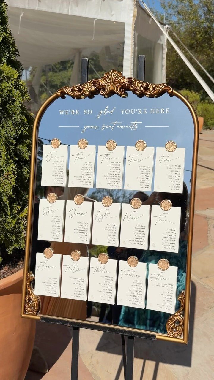 Ornate gold mirror seating chart with white cards and gold wax seals outdoors.