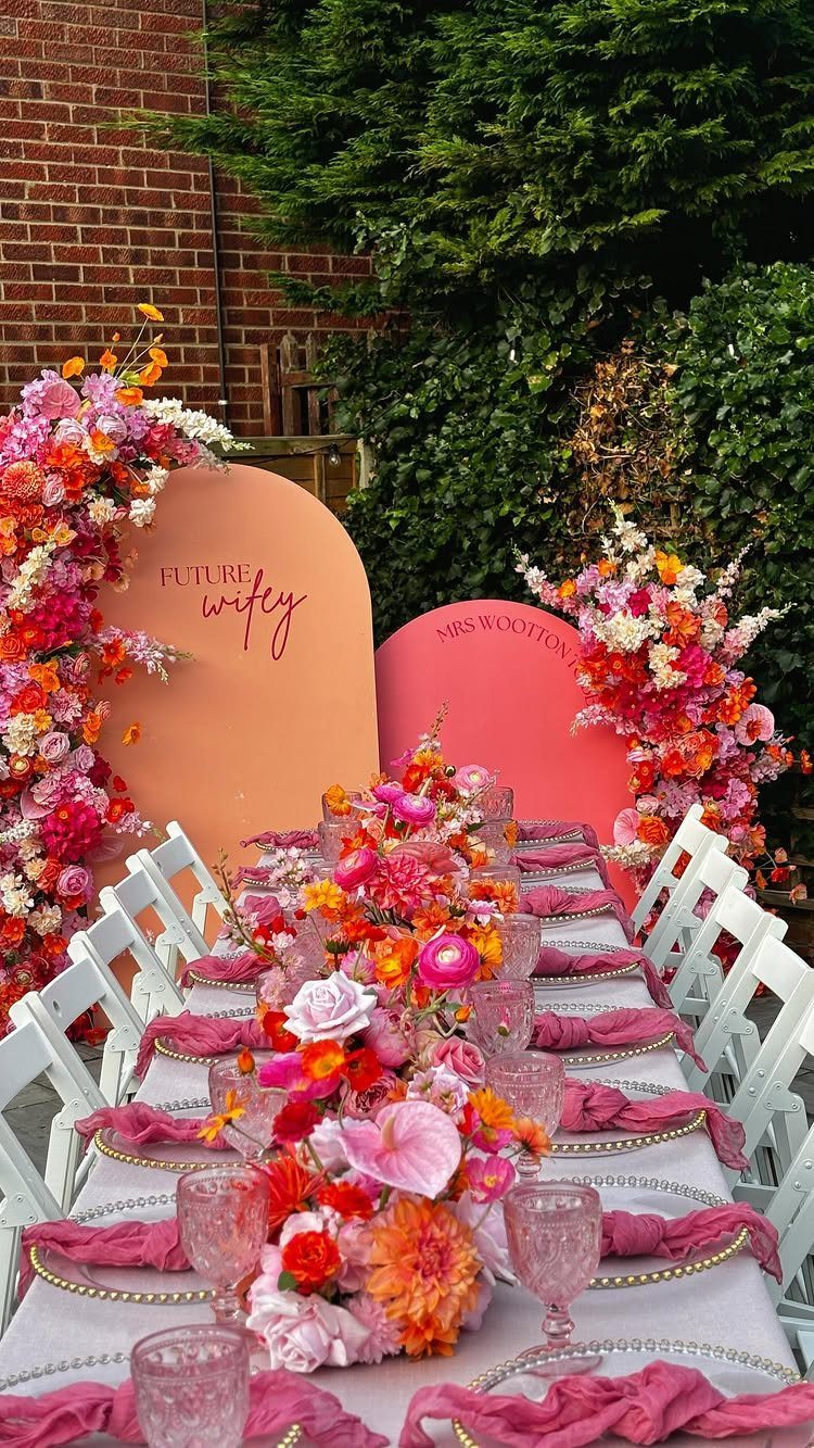 Decorated outdoor dining table with pink flowers and peach arched backdrops for celebration.