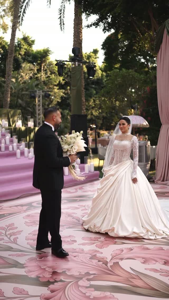 Groom in tuxedo and bride in white gown facing each other outdoors