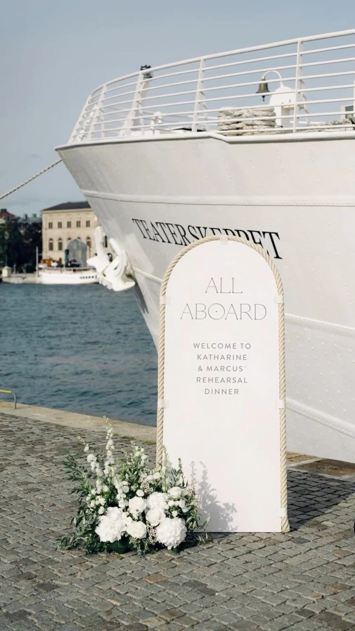 White arched welcome sign for a rehearsal dinner on a cobblestone dock by a ship