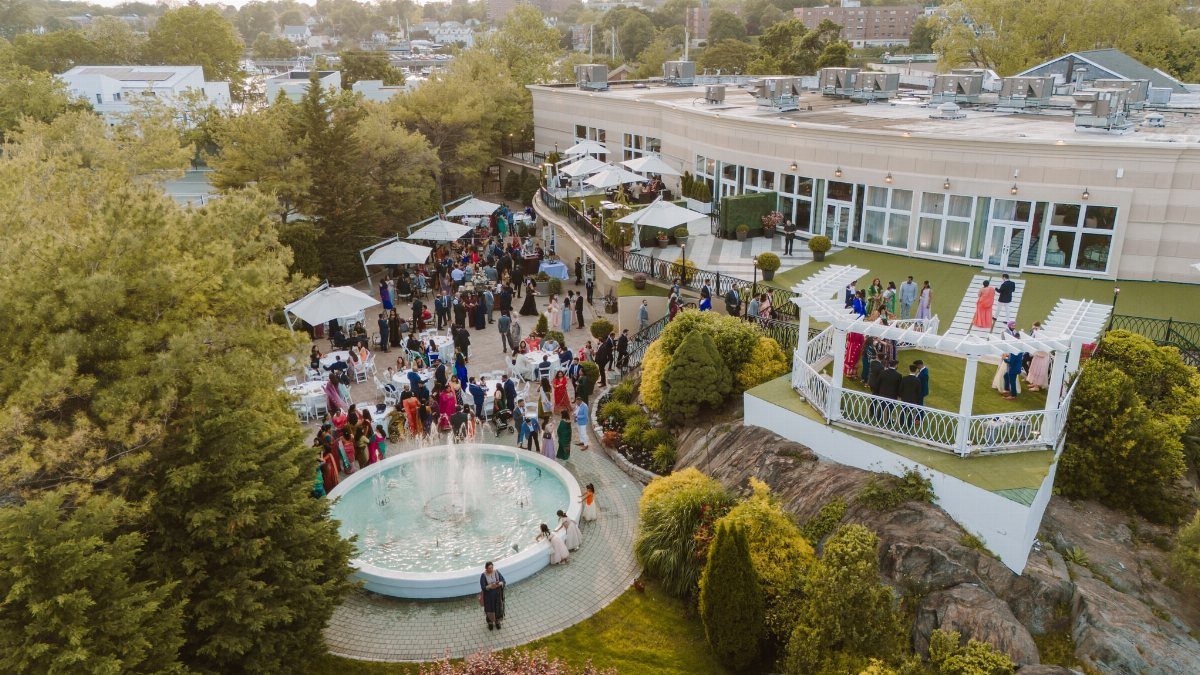 Outdoor gathering with guests around a fountain and white gazebo at a venue.