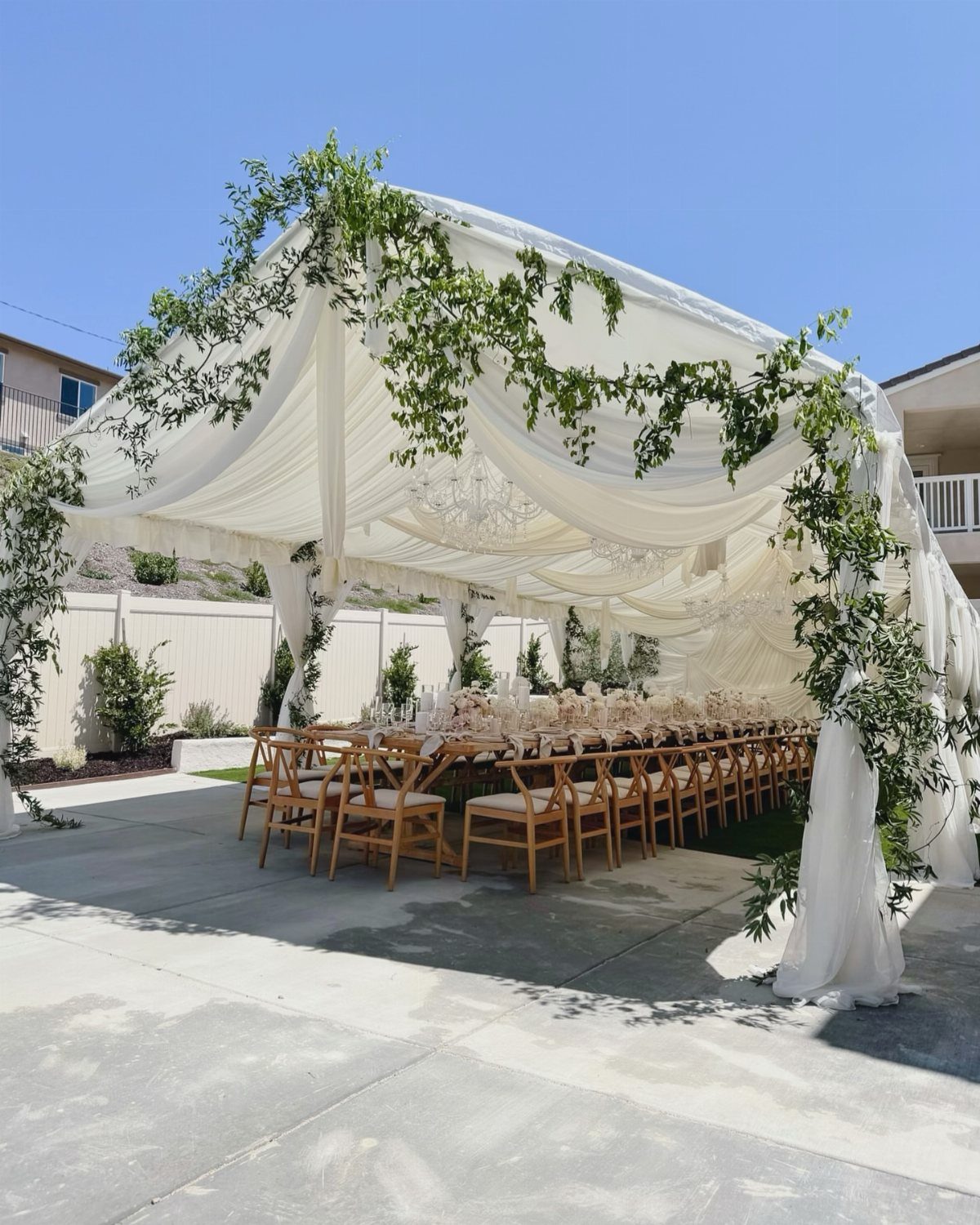 White draped tent with greenery over a long wedding dining table and chairs.
