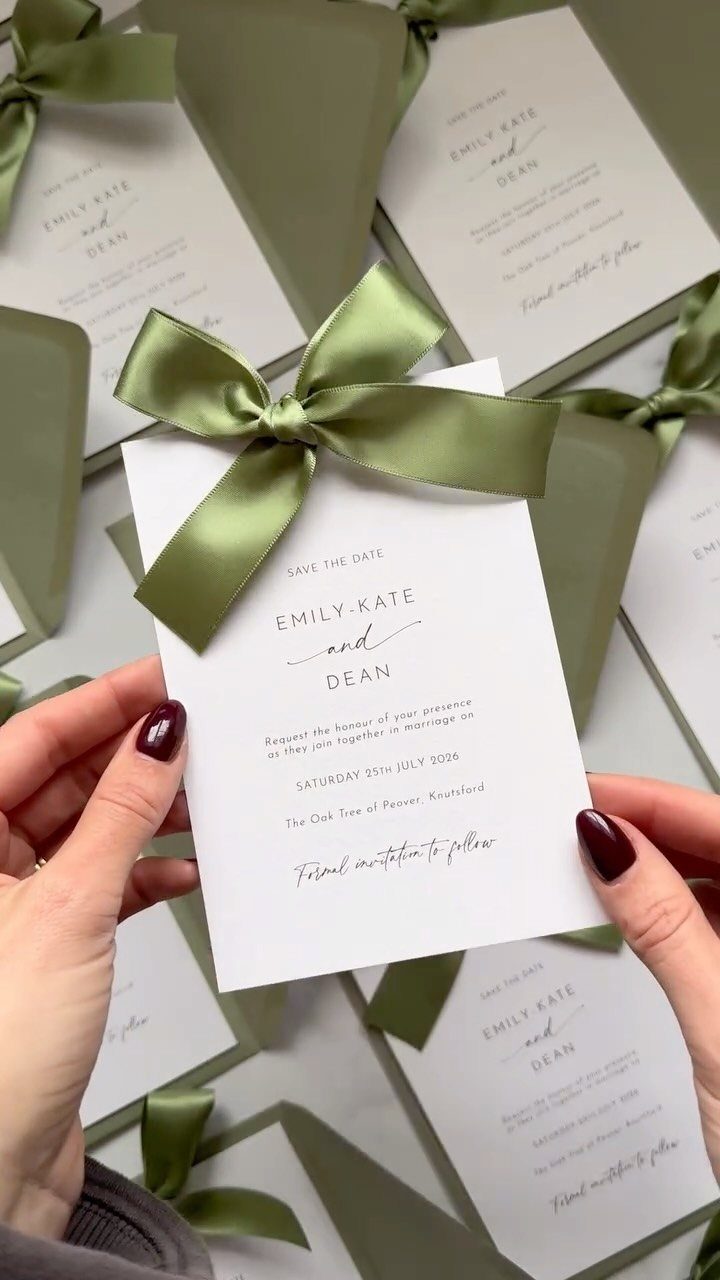 Wedding save the date cards with sage green satin bows and matching envelopes.