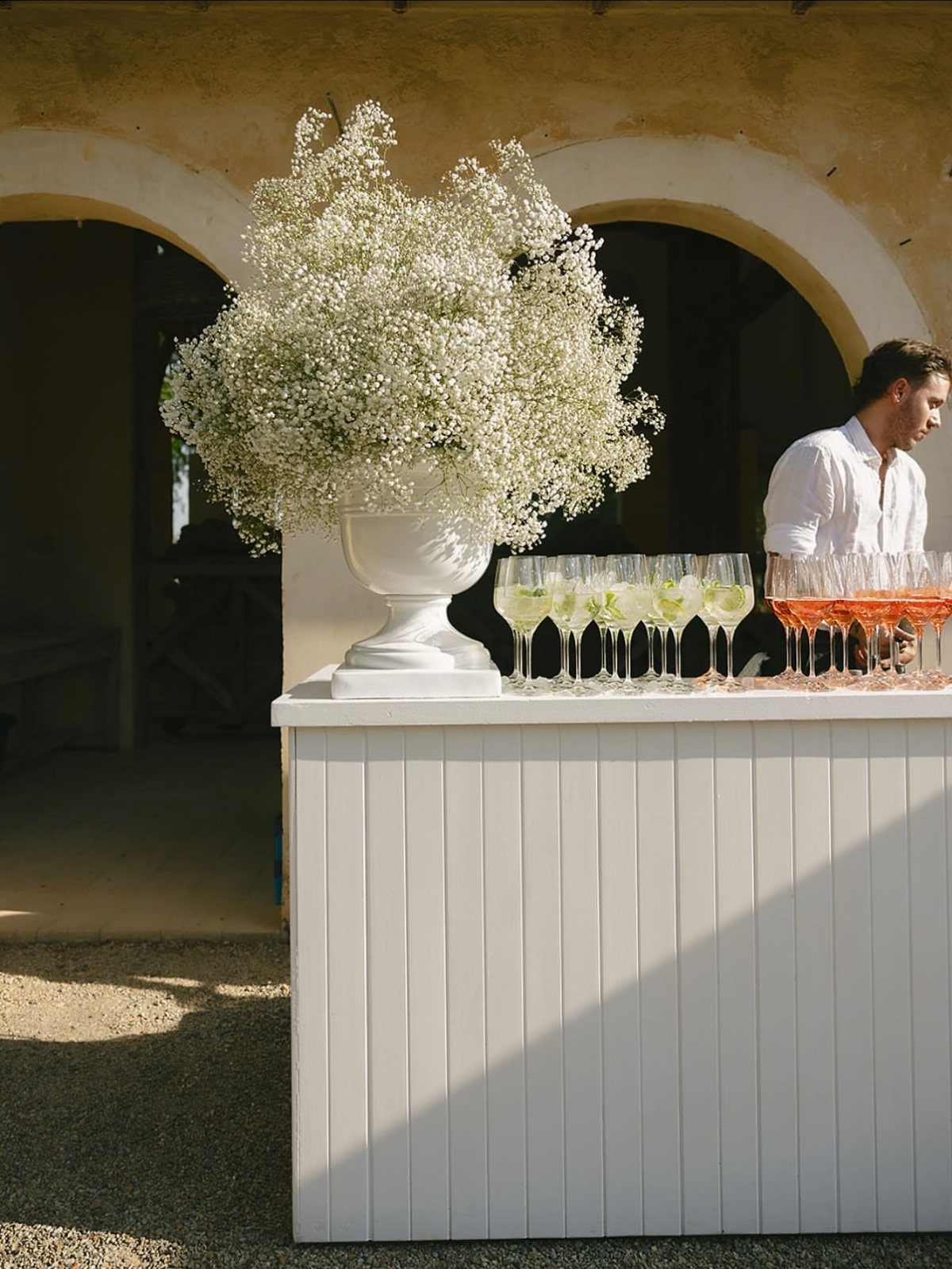 White bar counter with baby's breath floral arrangement and rows of colorful cocktails.