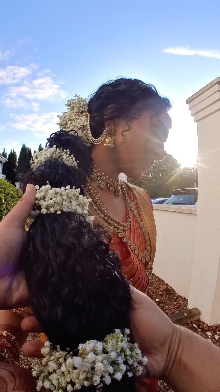 Woman's braided hair decorated with white flowers and traditional gold Indian jewelry.