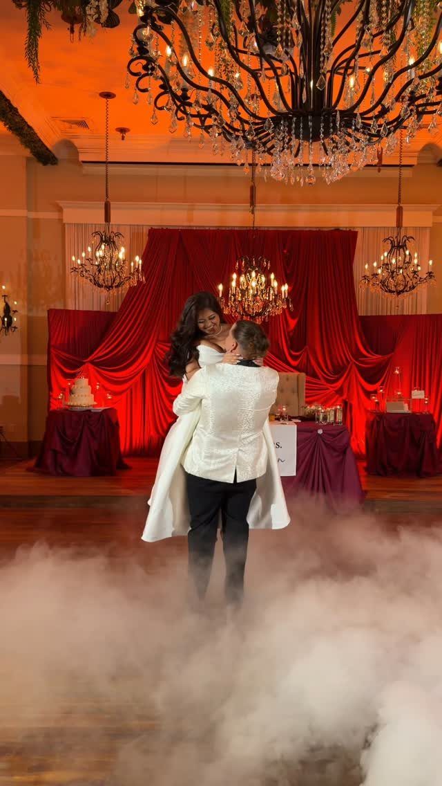 Couple dancing in a ballroom with white fog and red curtain backdrop.