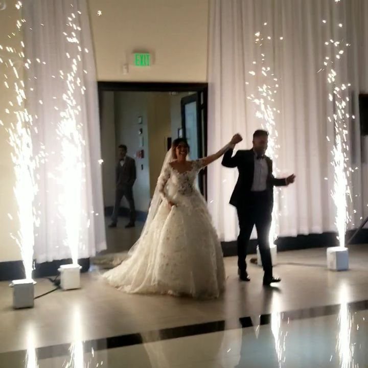 Bride and groom entering a reception hall between two indoor sparkler fountains.