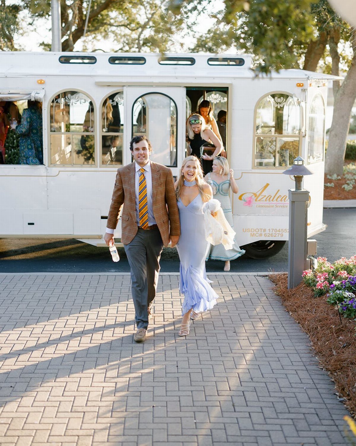 Couple walking hand-in-hand away from a white vintage trolley on a brick path