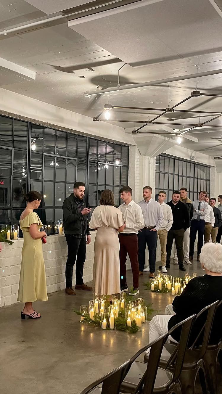 Wedding party practicing a ceremony in a white room with candlelit floor arrangements.