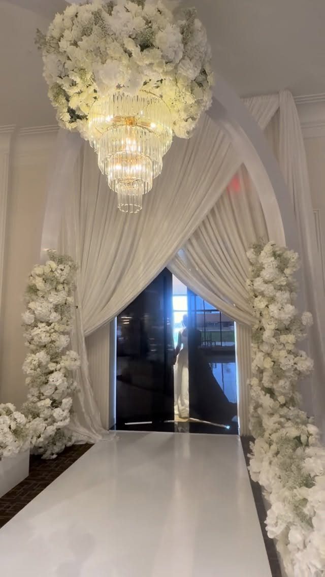 White floral arrangements decorating a wedding aisle with draped fabric and a chandelier.