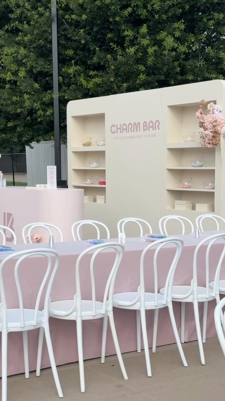Charm bar event setup with pink table, white chairs, and cream display backdrop.