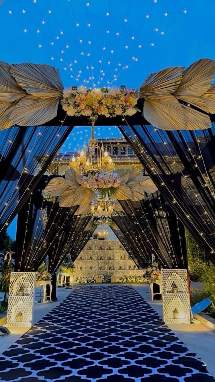 Elegant outdoor event entrance with black drapery, chandeliers, and a patterned floor runner.