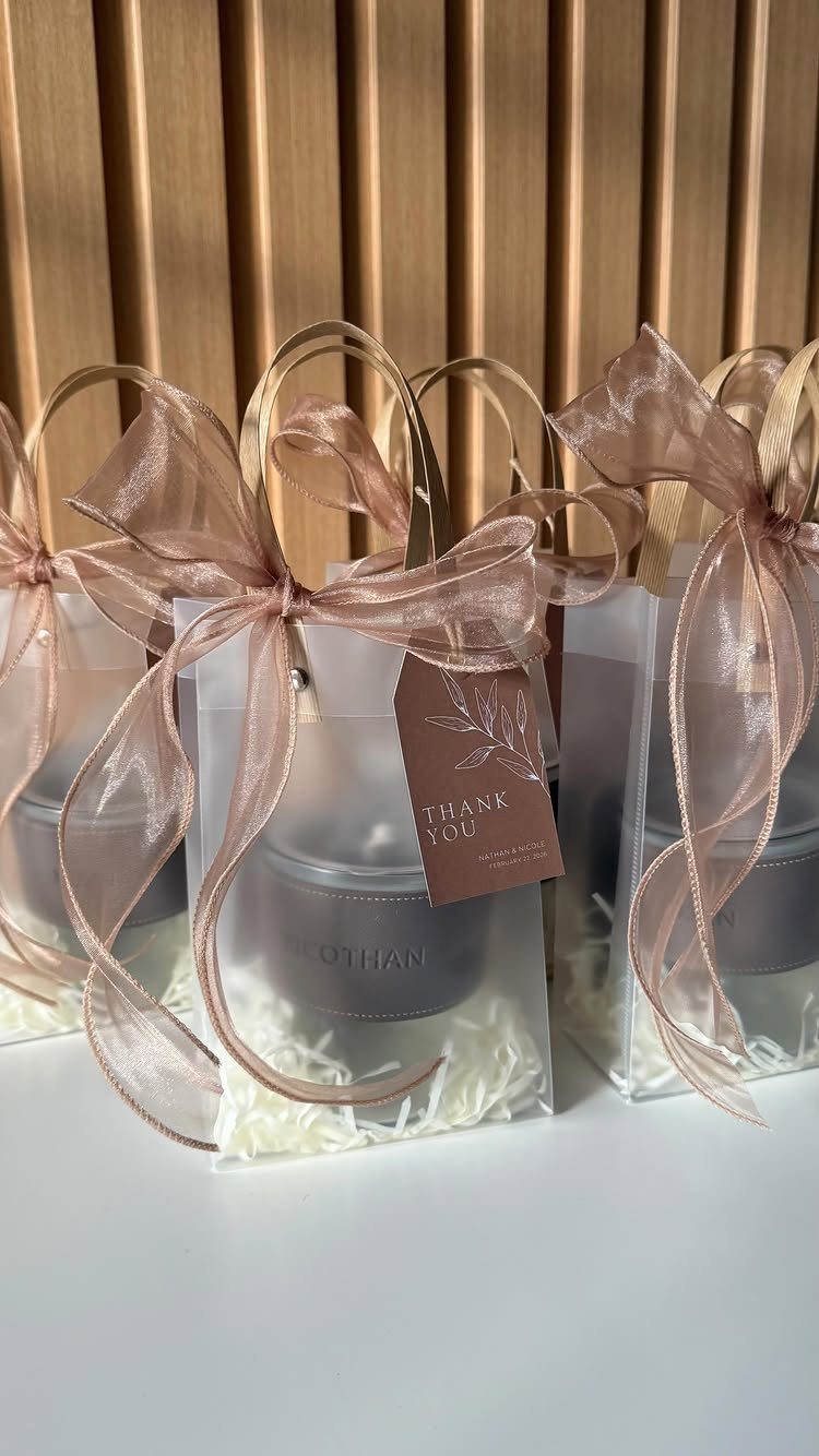 Wedding favor gift bags with grey candles, rose-gold ribbons, and thank you tags.