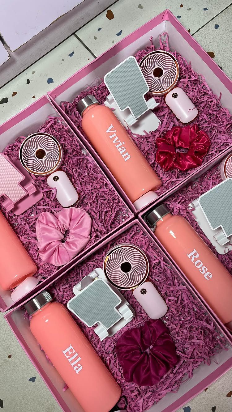 Four pink gift boxes containing personalized water bottles, scrunchies, and mirrors for bridesmaids.